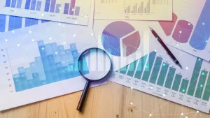Various charts and graphs on a desk with a magnifying glass sitting on top of them.